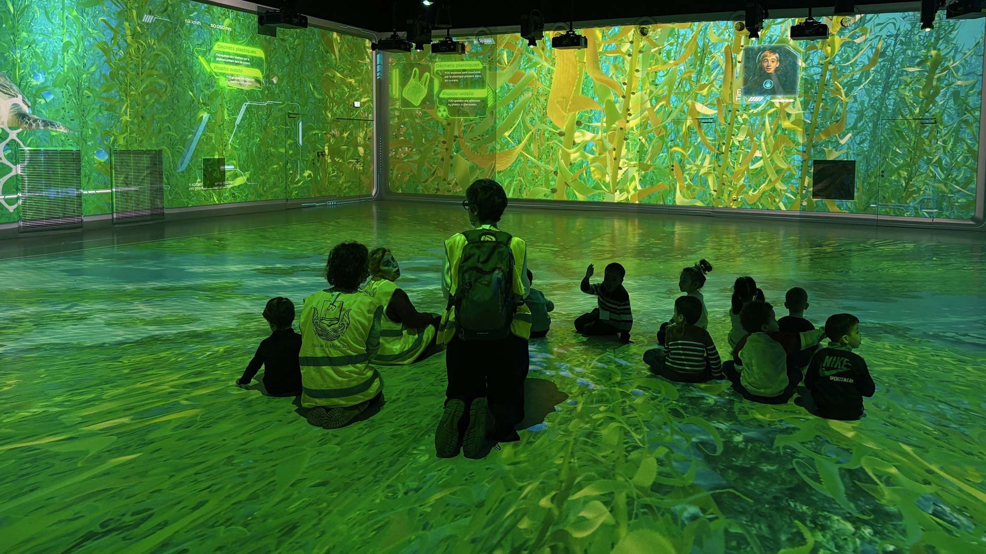 School group seated inside Ocean 360 immersive projection room with seaweed environment at Aquarium de Lyon