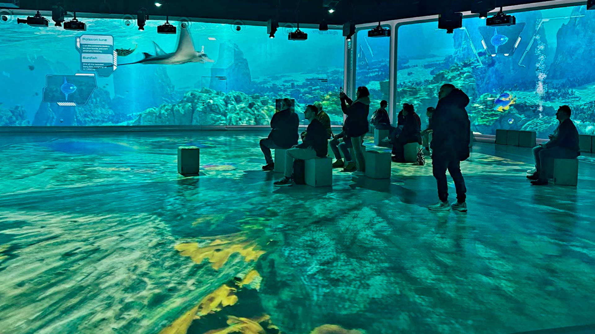 Visitors immersed in 360-degree underwater projection across walls and floor at Ocean 360, Aquarium de Lyon