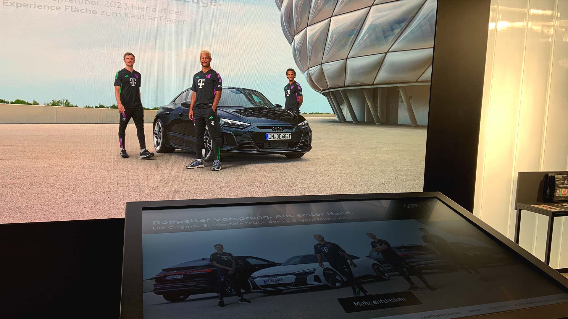 Large-format LED videowall displaying Audi FC Bayern campaign with interactive touch kiosk in foreground at FCBayern World Munich