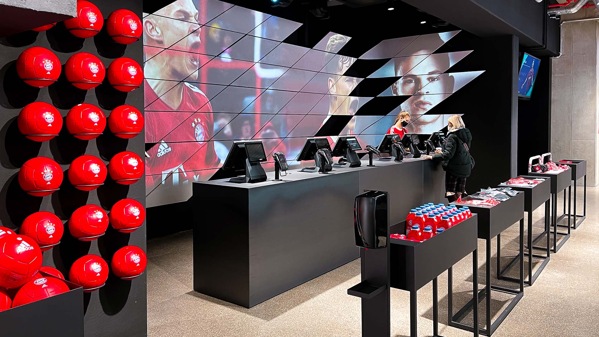 Checkout counter at FC Bayern World Munich with large-format LED video wall and branded digital displays