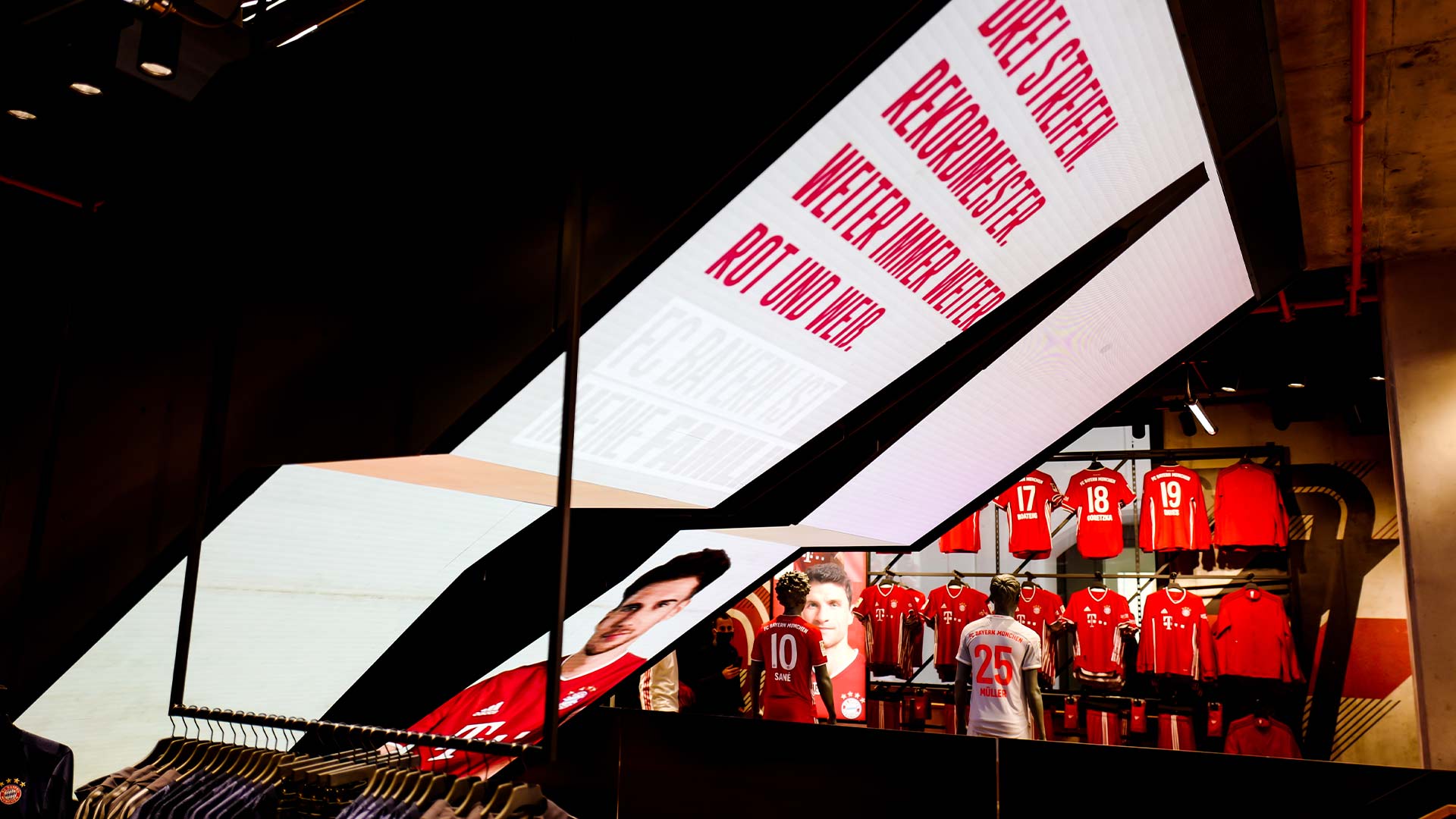 Diamond-shaped LED ceiling playing branded content above retail staircase at FC Bayern World flagship store in Munich