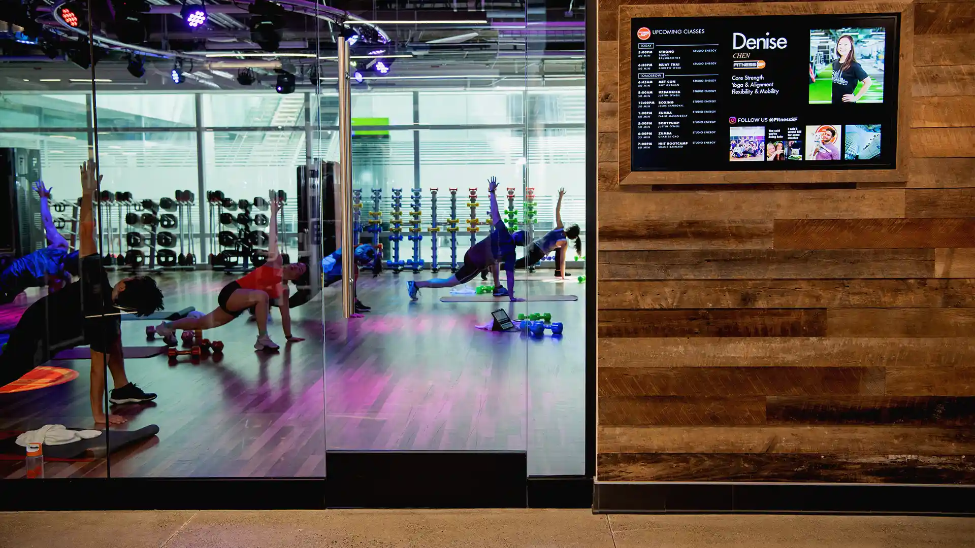 Große Videowand in einem Fitnessstudio von Fitness SF, auf der dynamische Trainingsinhalte und Community-Informationen angezeigt werden.