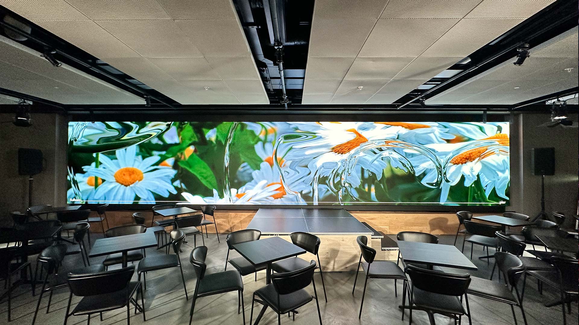 Wide-angle LED wall displaying floral digital content in the Riverside Market bar at Fulham Pier, London
