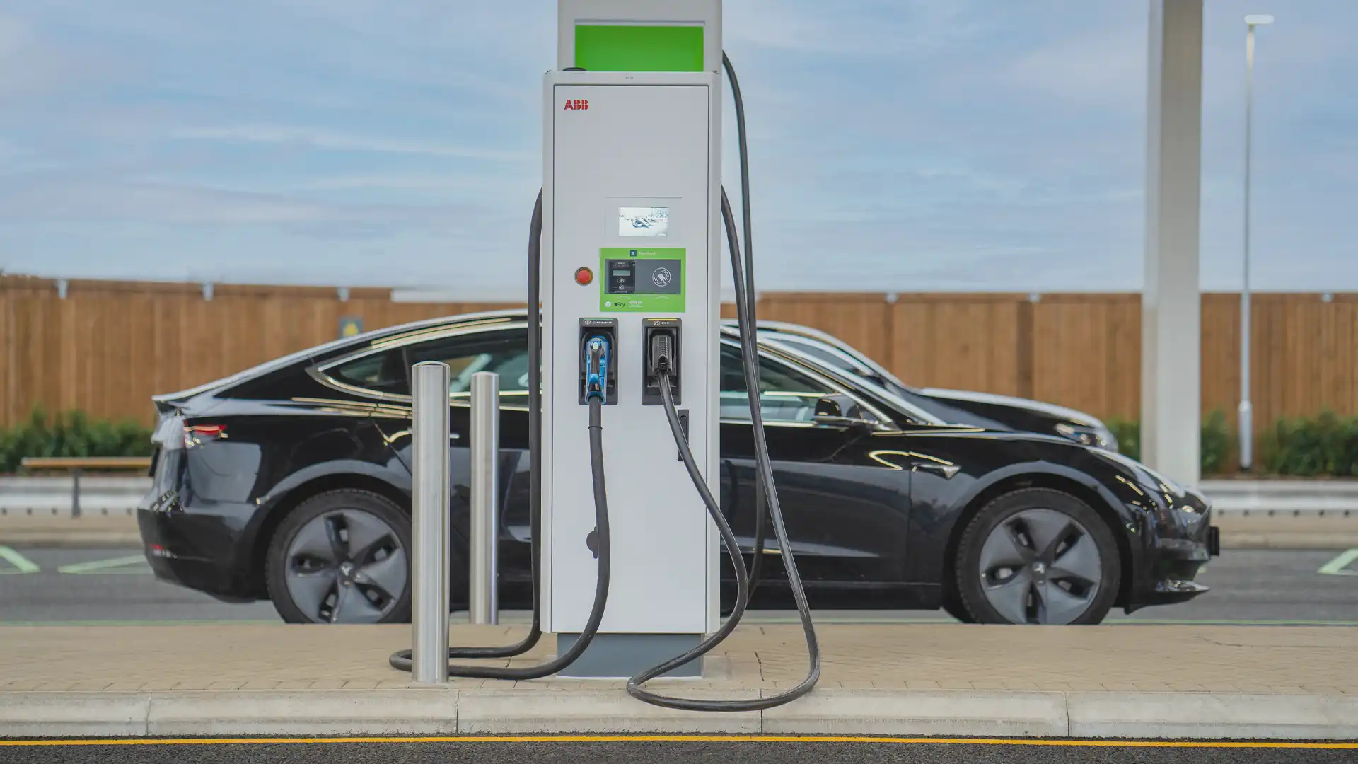 Chargement de véhicules électriques au GRIDSERVE's Electric Forecourt®, avec affichage numérique intégré près de la borne pour améliorer l'expérience de l'utilisateur et mettre en avant la mobilité durable.