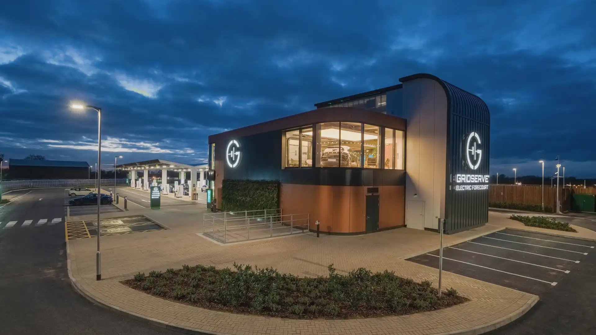 Vue extérieure de l'Electric Forecourt® de GRIDSERVE à Braintree, avec signalisation numérique et écrans LED architecturaux intégrés dans la conception durable de la station.