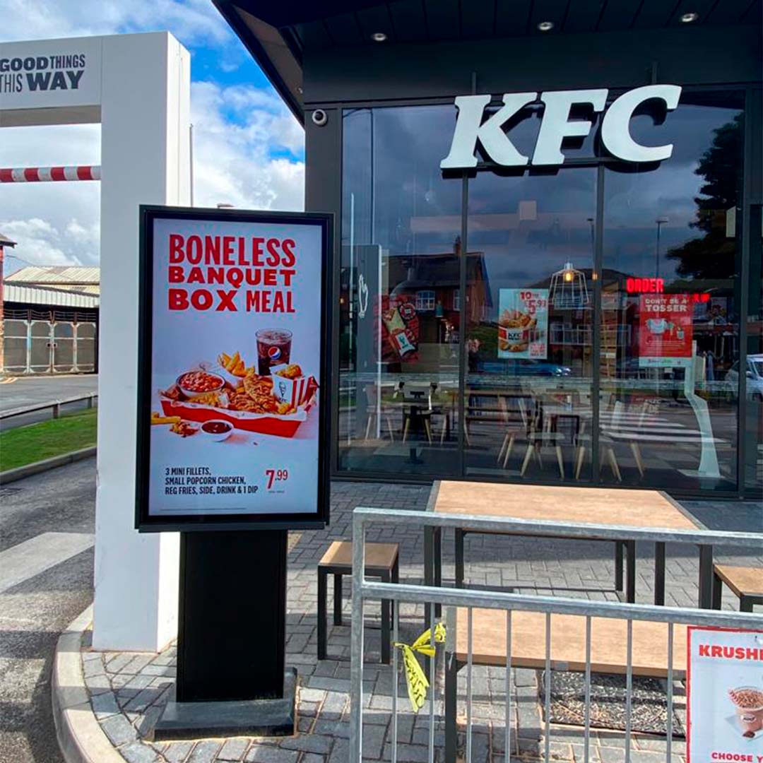 Freestanding digital totem displaying a KFC menu promotion outside a restaurant entrance in the UK