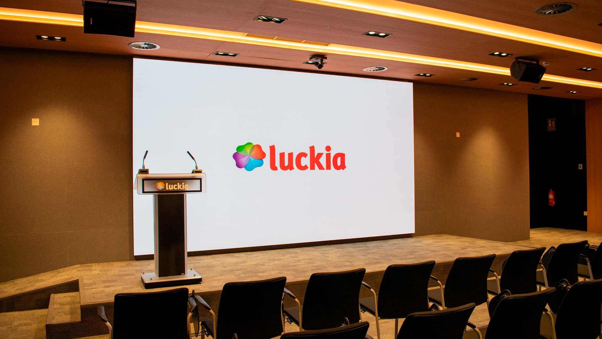 Seitenansicht des Luckia-Auditoriums mit LED-Bildschirm, Säulenlautsprechern und Rednerpultmikrofonen, integriert von TRISON in A Coruña