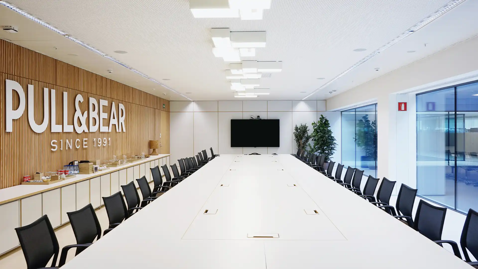 Détail de l'aménagement des bureaux Pull&Bear où les écrans LED et les systèmes audio sont intégrés dans le mobilier pour une esthétique minimaliste.