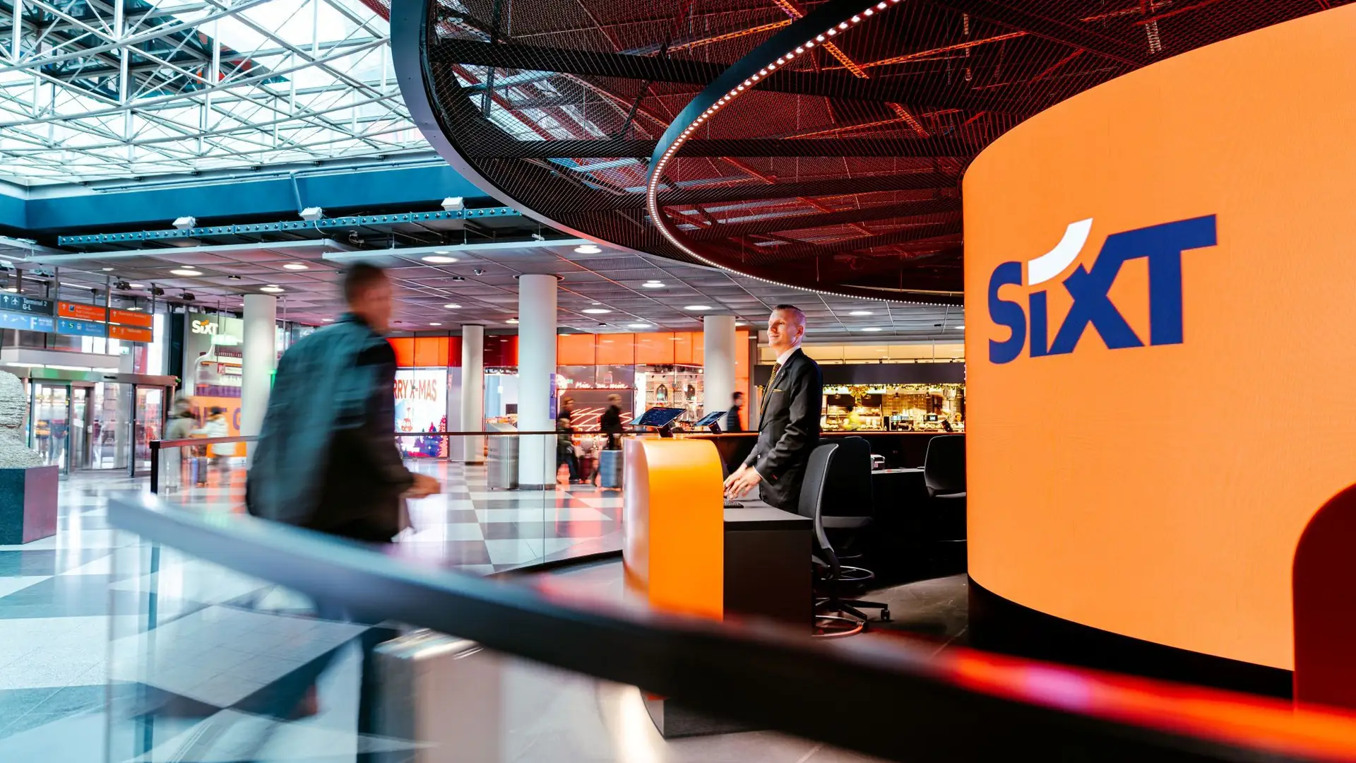Traveller passing the SIXT rental counter under the LED ring at Munich Airport