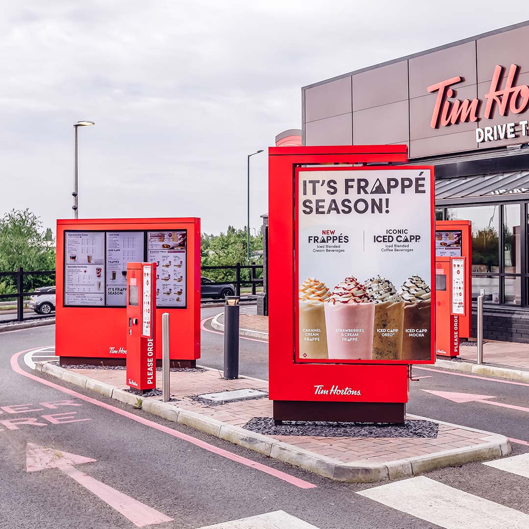 Quiosco digital rojo drive-thru y pantalla promocional de Tim Hortons instalados en exterior de restaurante UK