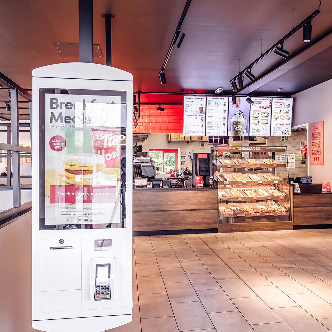 Quiosco de autoservicio blanco en Tim Hortons UK con pantalla táctil y lector de pago sin contacto